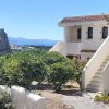 Casa bianca su scala, vegetazione e mare sullo sfondo.