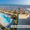 Piscina e spiaggia soleggiata con ombrelloni.