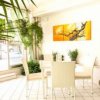 Area interna luminosa con tavolo, sedie bianche e piante. Quadro giallo sulla parete.