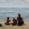 Due bambini e un adulto seduti sulla spiaggia guardano il mare.