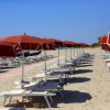 File di lettini e ombrelloni rossi su una spiaggia sabbiosa.