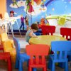 Bambino seduto a un tavolo circondato da sedie colorate in una sala giochi.
