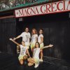 Cinque persone sorridenti posano davanti a un palco con insegna Magna Grecia.