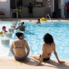 Due donne in bikini sedute a bordo piscina, persone nuotano nello sfondo.