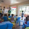Aula con bambini seduti a tavoli colorati.