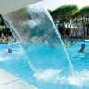 Piscina affollata con getti d'acqua e alberi.
