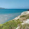 Spiaggia con bagnanti e promontorio erboso.