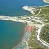 Visuale aerea di una spiaggia con ombrelloni e promontorio.