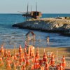 Spiaggia con ombrelloni e struttura in legno su roccia.