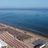 Spiaggia con file ordinate di ombrelloni e lettini, fronteggiando il mare calmo.