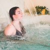Donna rilassata sotto getto d'acqua in piscina.